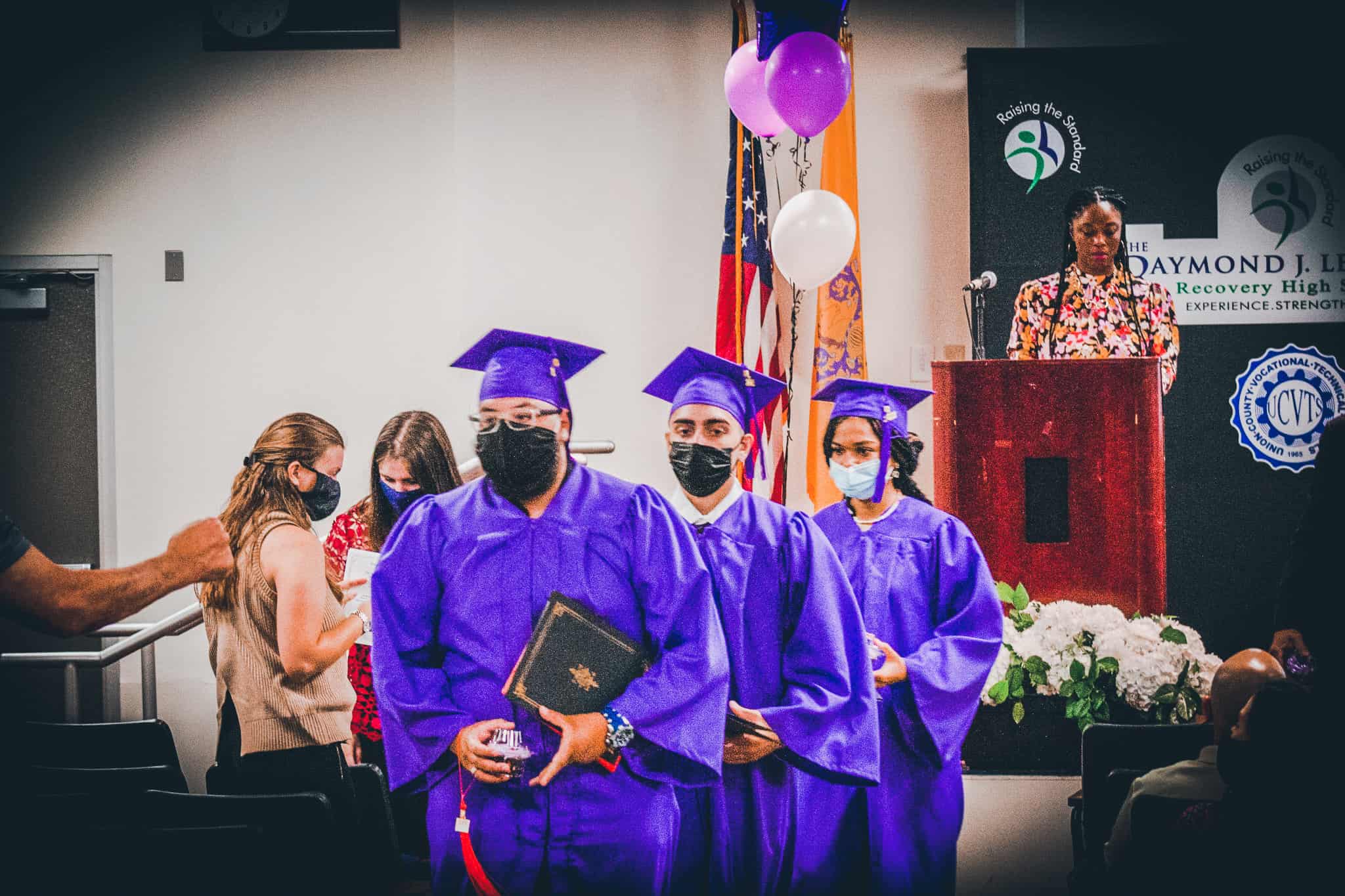 Recovery high school graduates walk down from the stage with diplomas