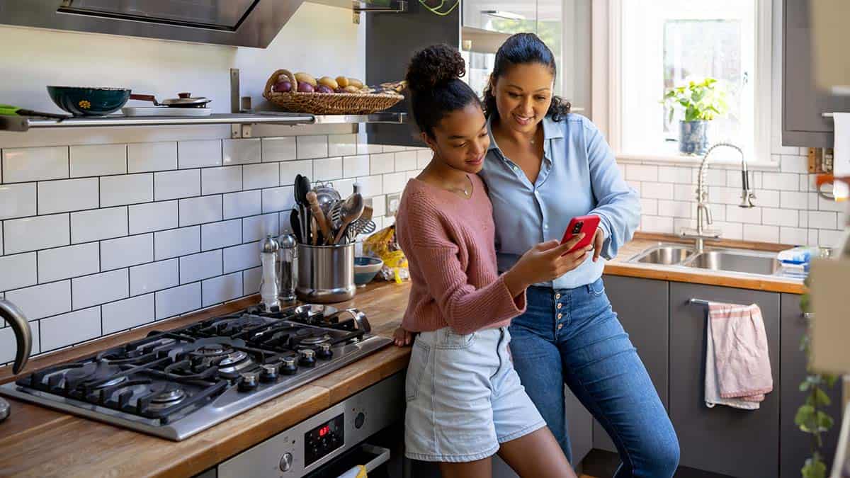 A mother and daughter looking at the daughter's phone in the kitchen.