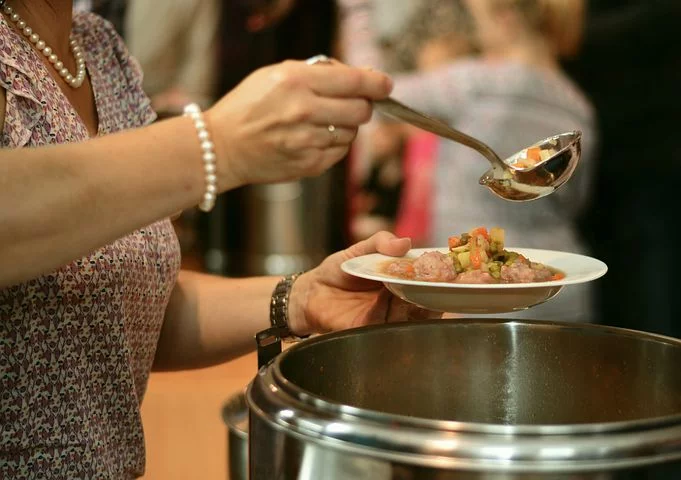 woman serving soup from a large pot