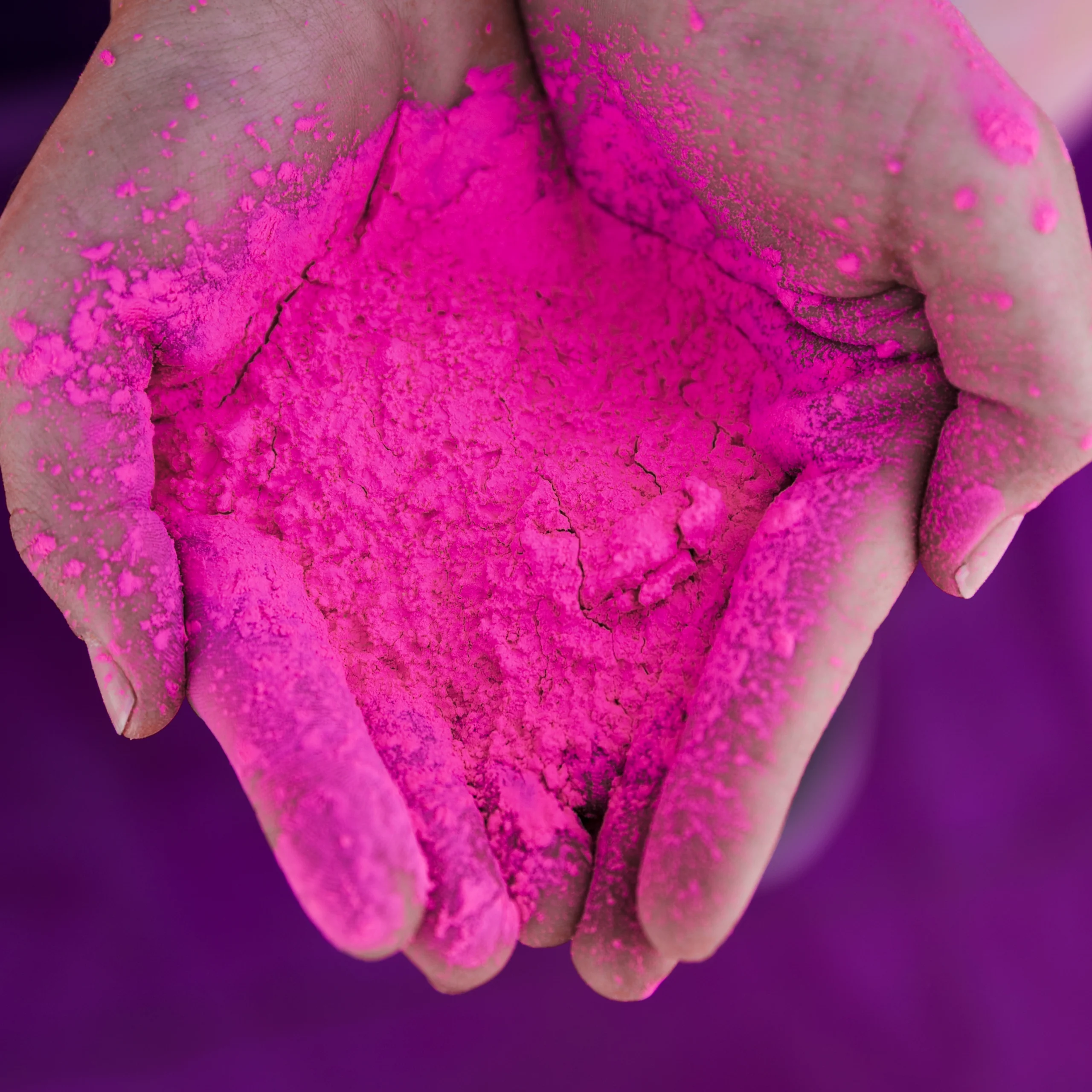 Hands with pink coloring on them in front of a purple background. Picture provided by Freepik